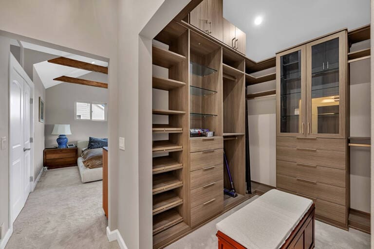 Large walk-in closet with wooden shelves, drawers, and glass cabinets.