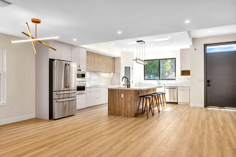 Modern kitchen with light wood floors, white cabinets, and a wooden island.