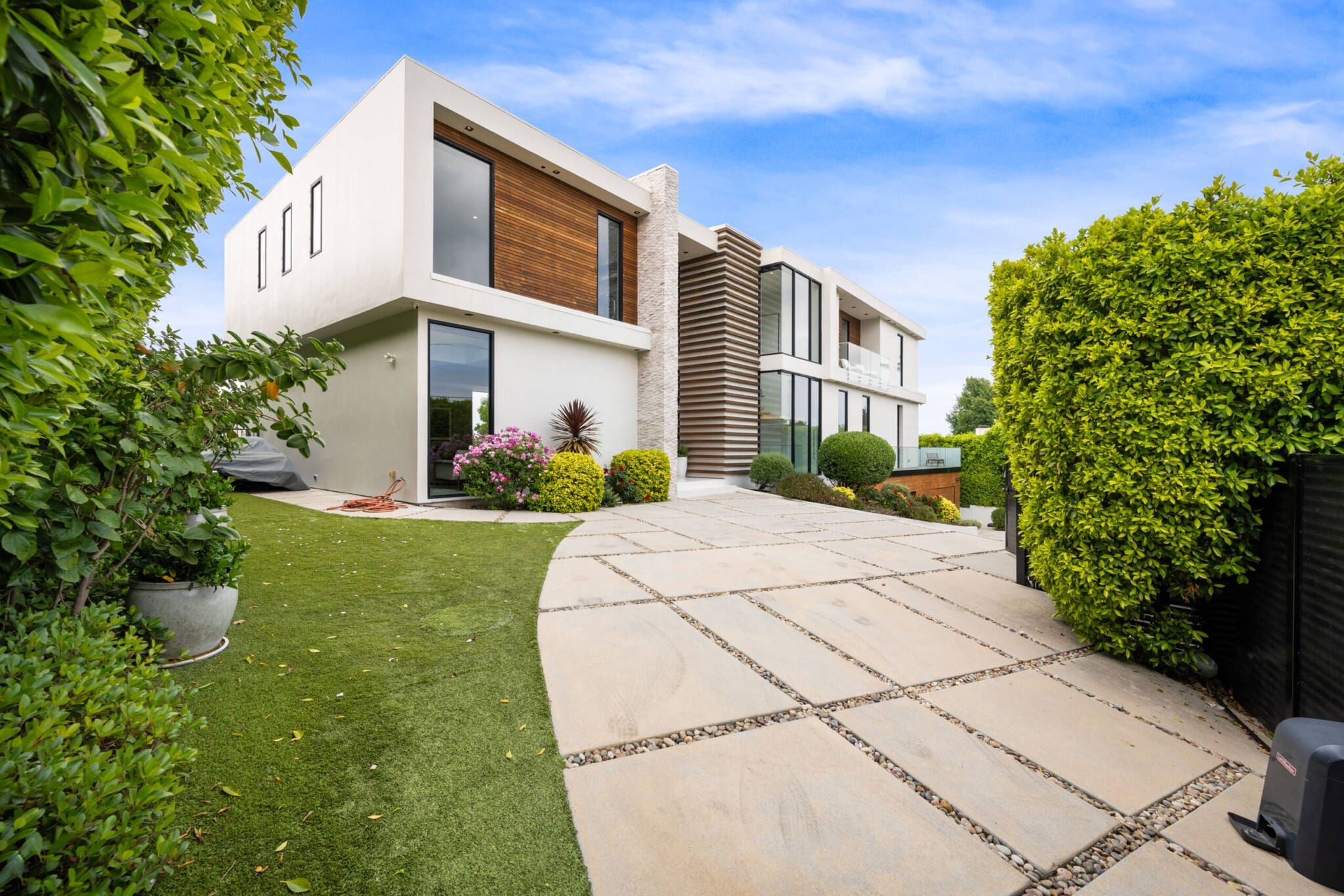 Modern white house with wood accents, large windows, and a paved driveway.