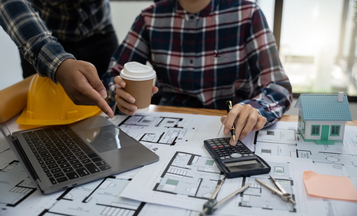 Two people working on house blueprints with a laptop and a calculator.