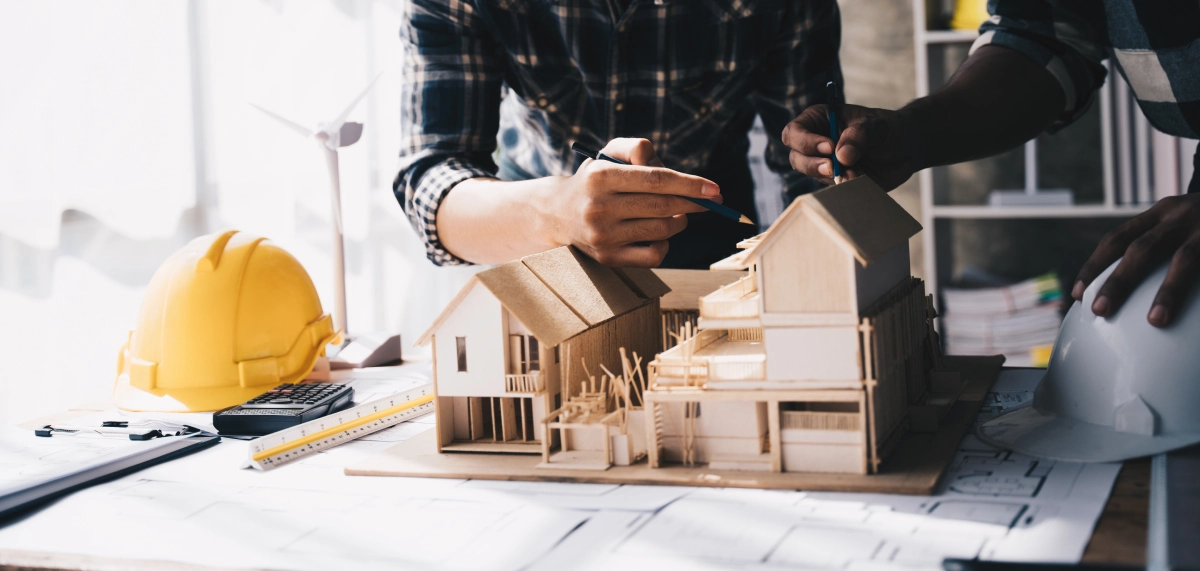 Architects working on a detailed wooden house model with hard hats nearby.