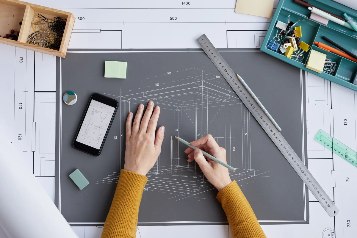 A person in a yellow sweater working on a technical drawing with a pencil.