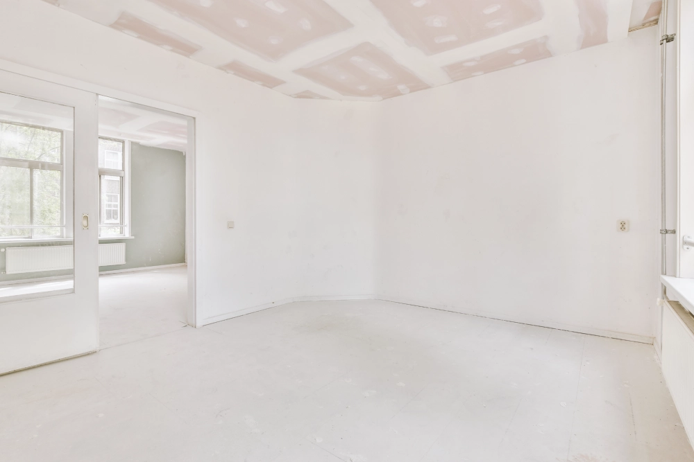 An empty room under renovation with white walls and a plastered ceiling.