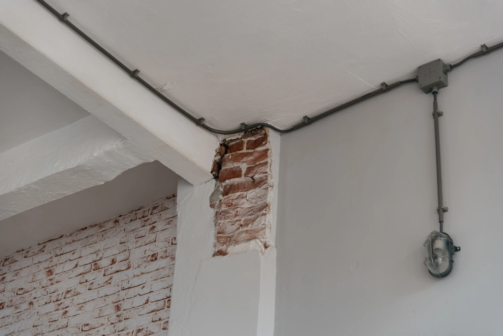 Damaged structural pillar showing red bricks underneath cracked white plaster.