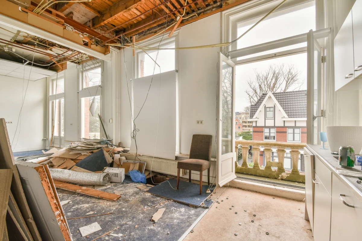 An interior room under renovation with exposed ceiling structures and debris on the floor.