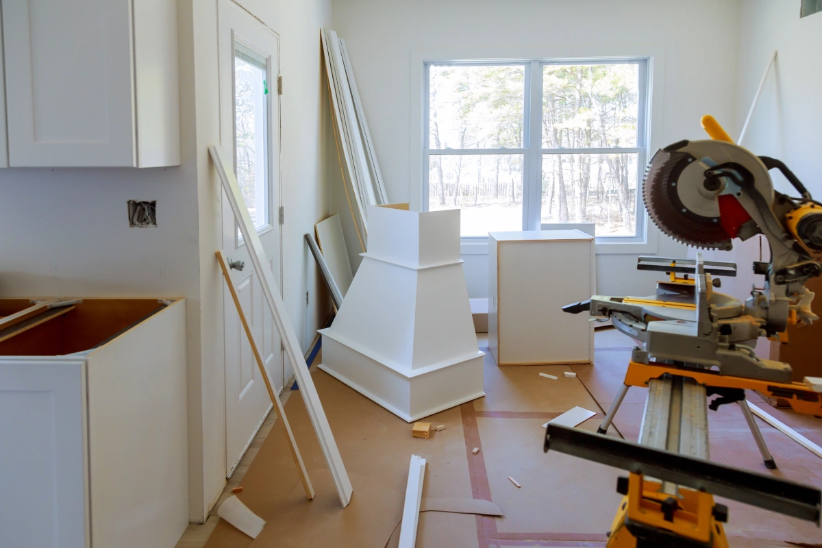 A white kitchen under renovation with a miter saw in the foreground and white cabinets.