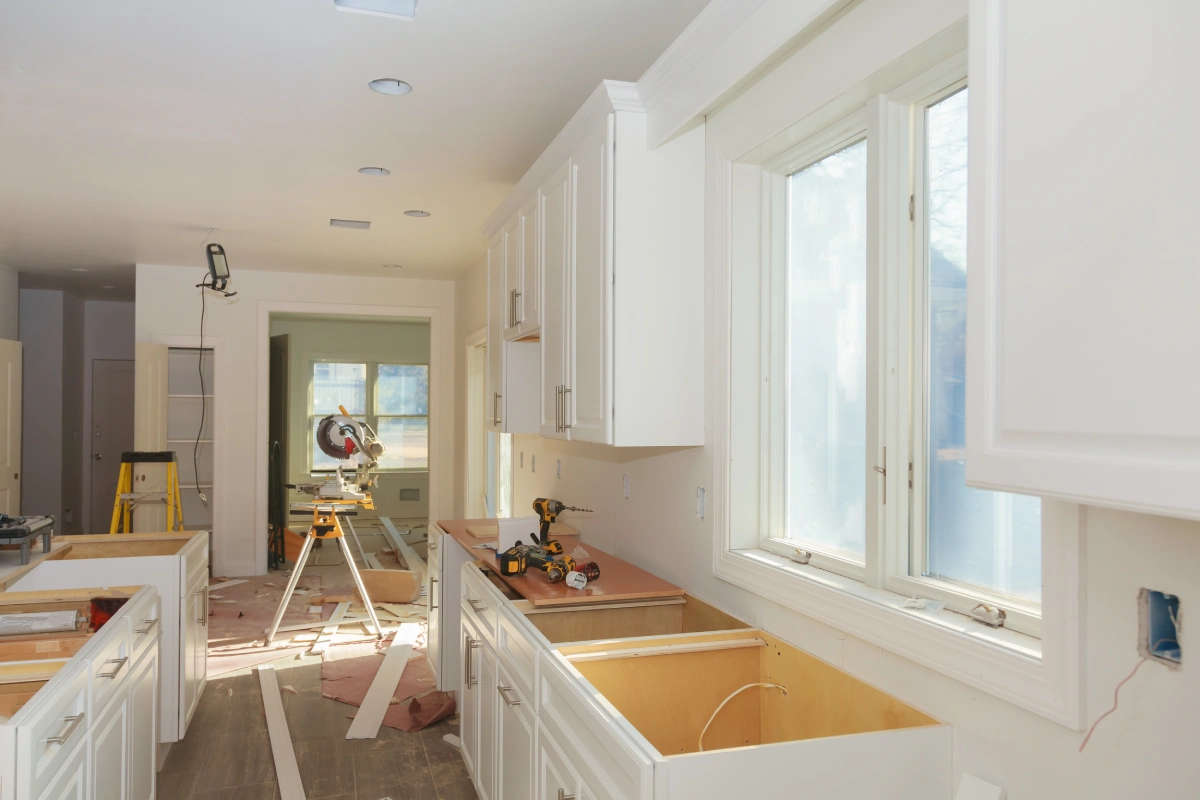 A modern kitchen undergoing construction with white cabinets and power tools.